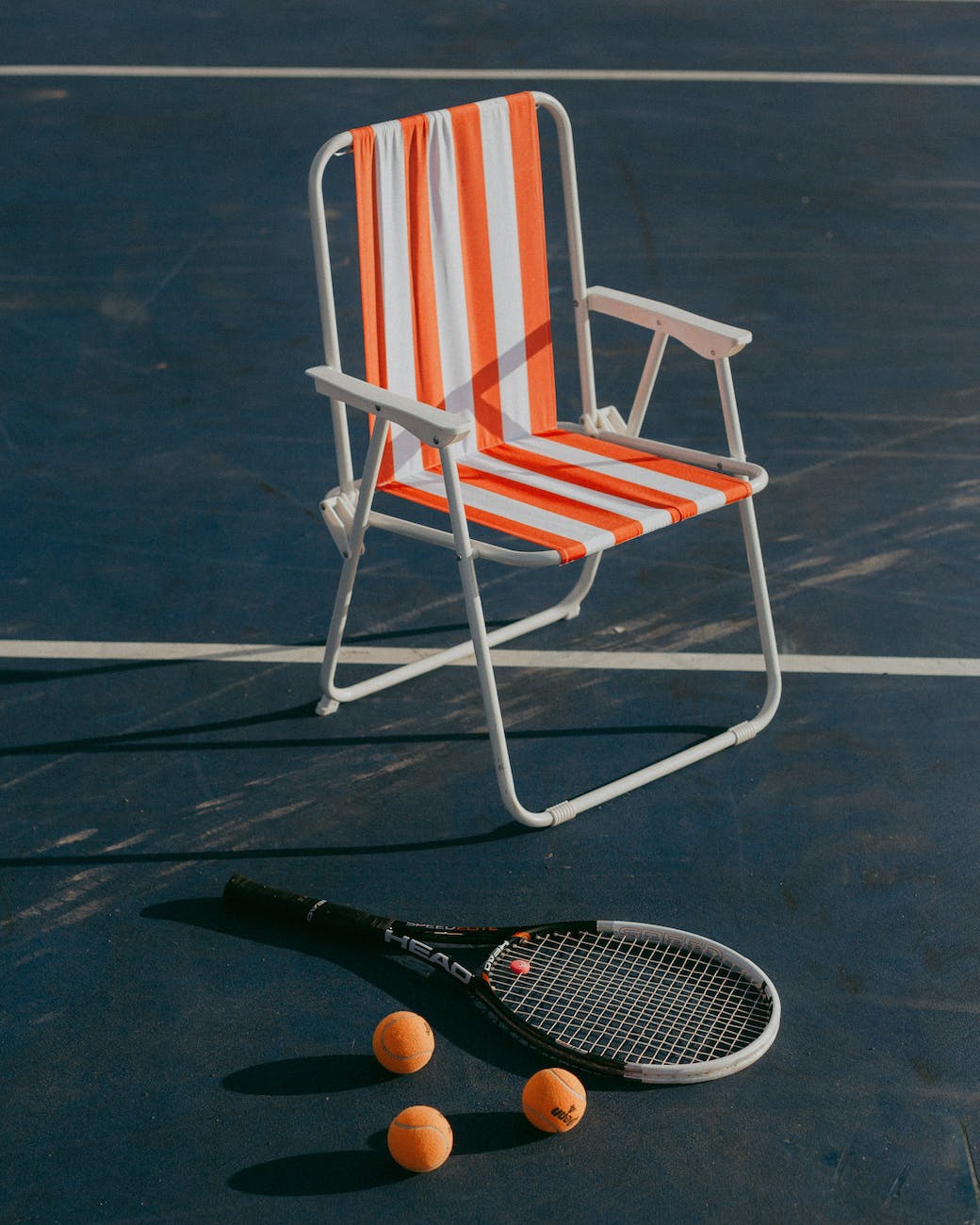 chair on tennis court next to racket and balls